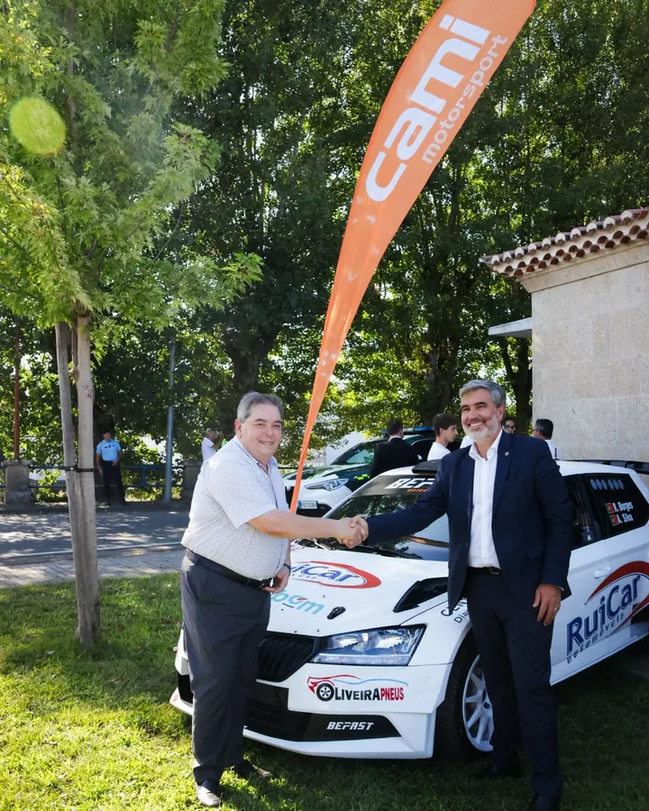 Aperta de mans entre representantes de CAMI Motorsport e da Eurocidade Chaves-Verín diante dun dos vehículos participantes.