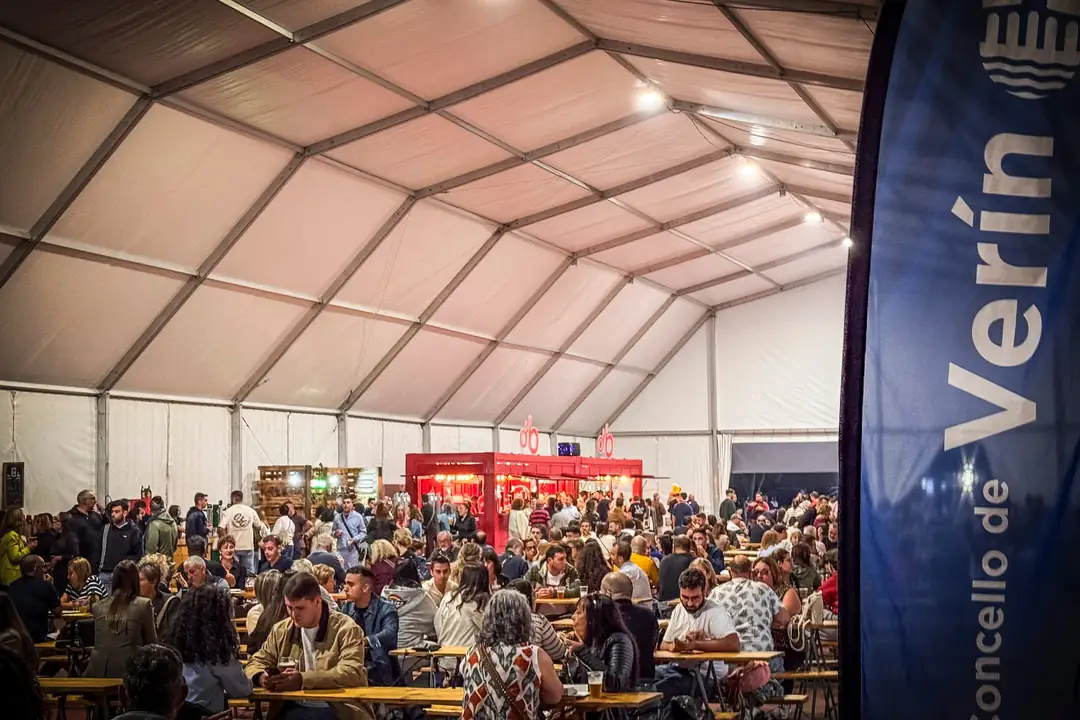 Interior da carpa principal da VI Festa da Cervexa de Verín, chea de público nas mesas corridas, cos postos cervexeiros ao fondo.