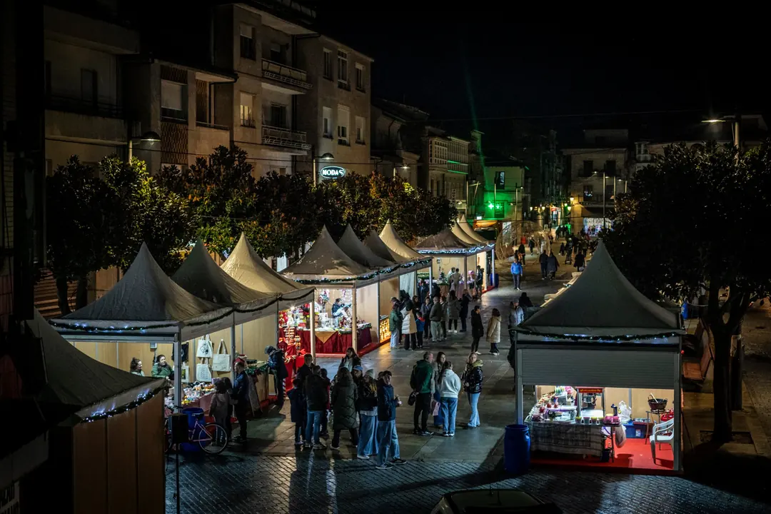 Casetas iluminadas da Feira de Nadal na Praza Maior de Verín, con público percorrendo os postos durante a noite.